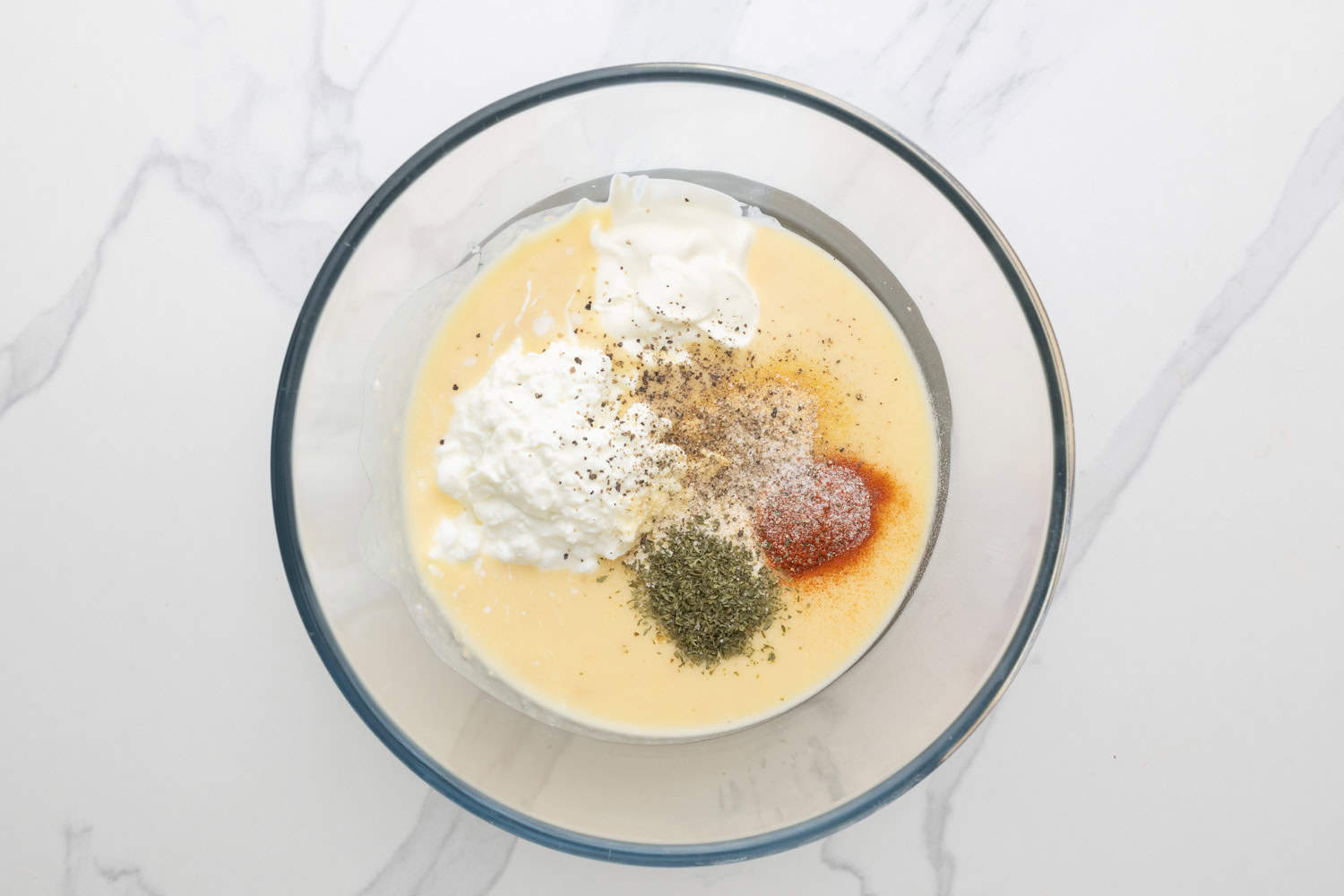 cream of chicken soup in a glass mixing bowl with seasonings, sour cream, and cottage cheese