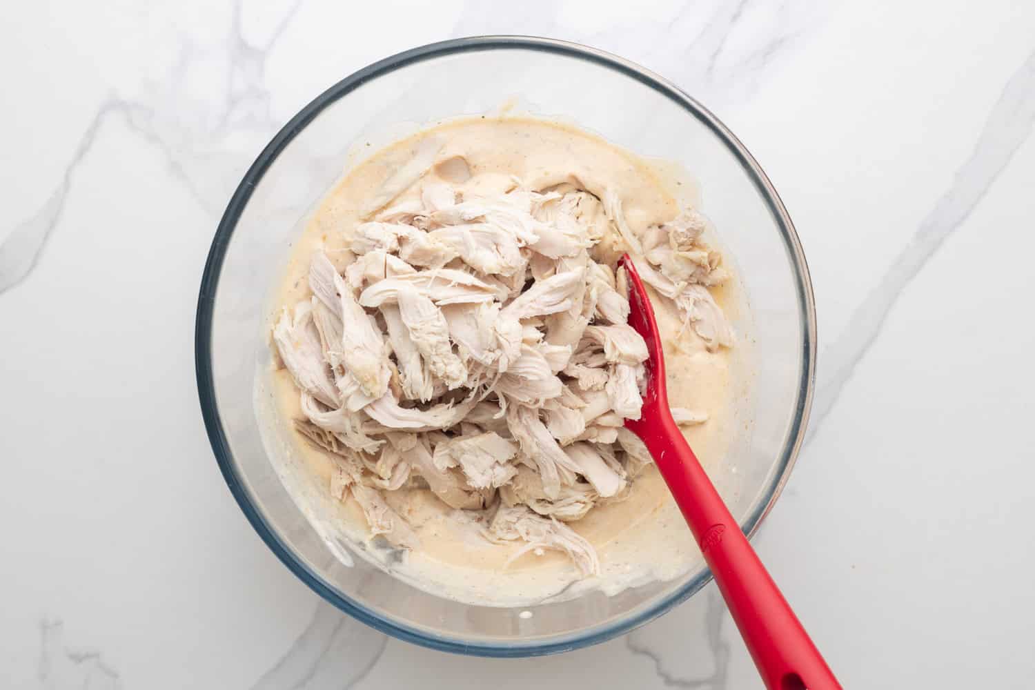 shredded rotisserie chicken added to creamy mixture in a glass bowl .