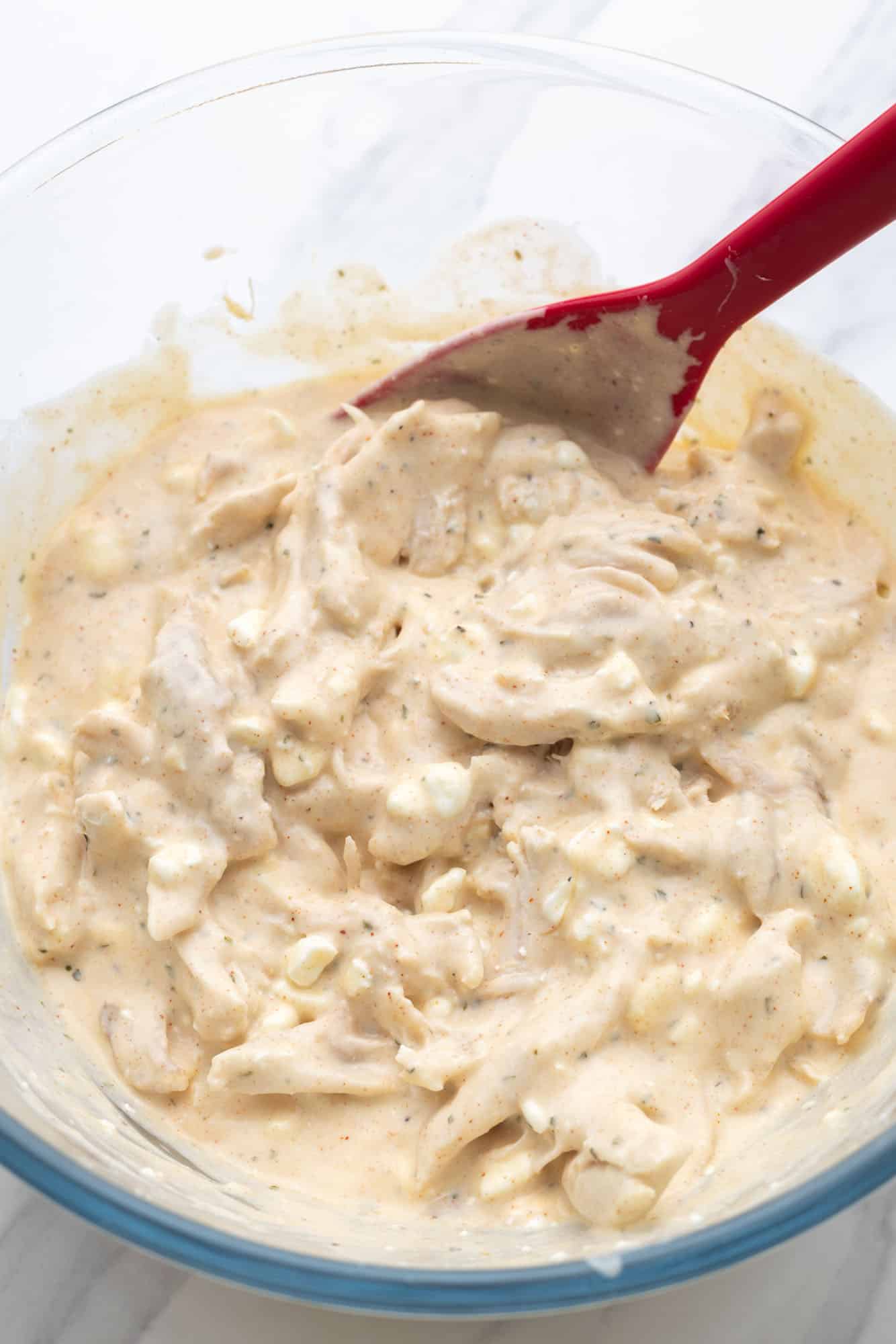 chicken in a creamy sauce in a glass bowl with a red spatula