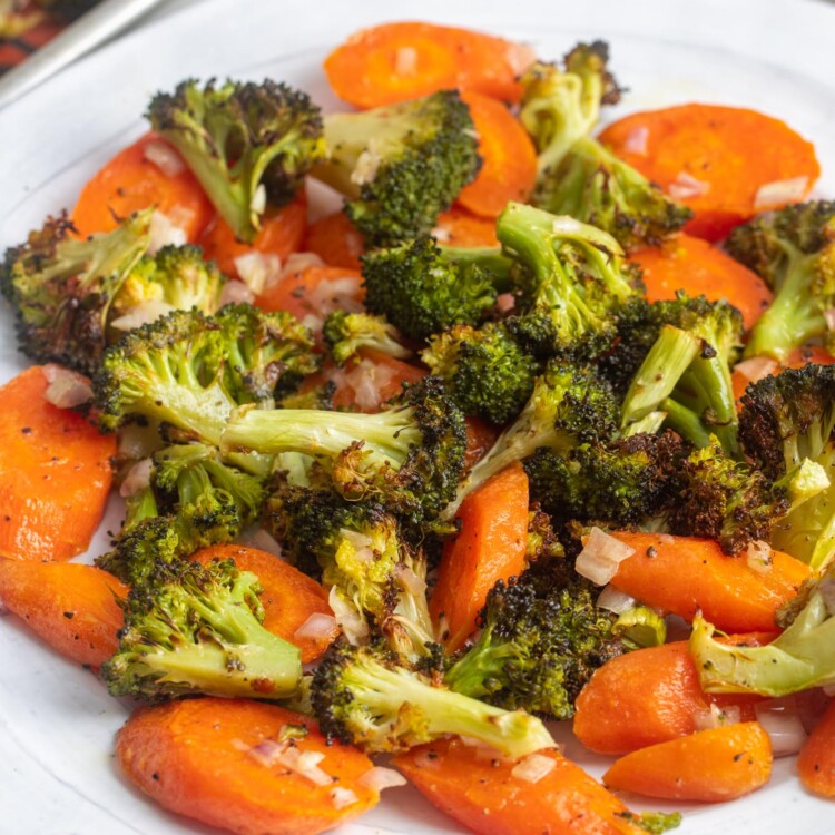 a white dinner plate with roasted sliced carrots and roasted broccoli .