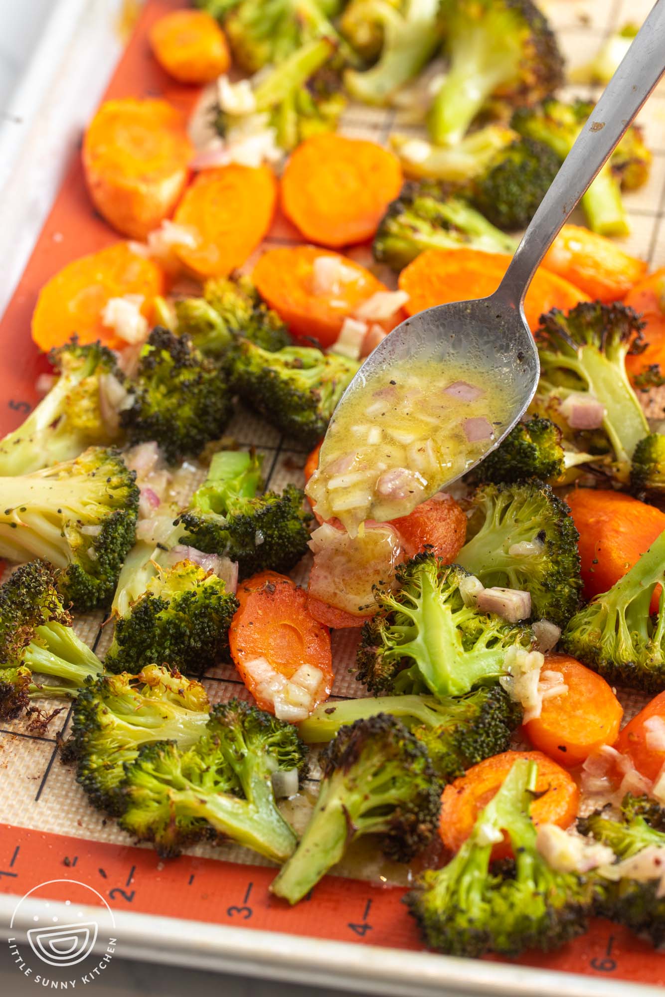 roasted carrots and broccoli on a silpat. a spoon is adding shallot butter sauce over the veggies.