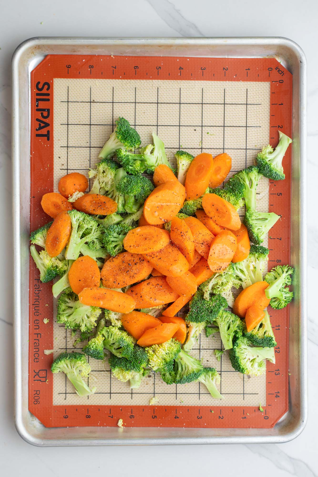 raw sliced carrots and broccoli on a silpat lined baking sheet, seasoned with salt and pepper.