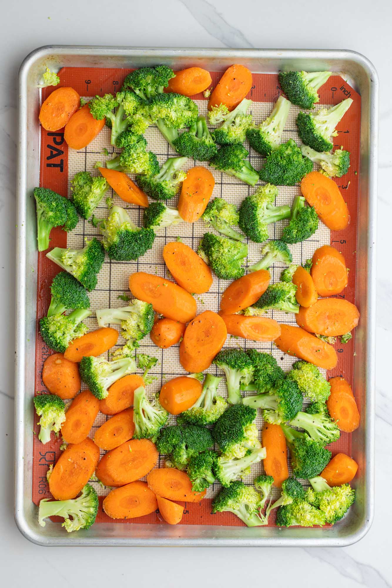 sliced carrots and broccoli florets on a silpat lined baking sheet, viewed from above