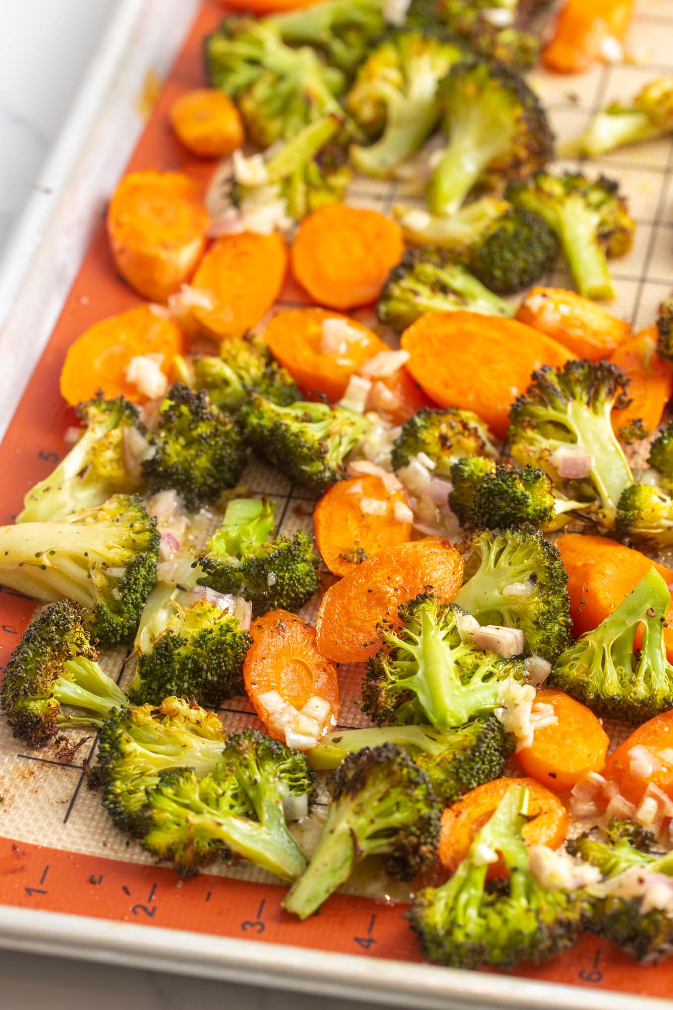 a grid silpat baking mat holding browned roasted broccoli and carrots, topped with shallots