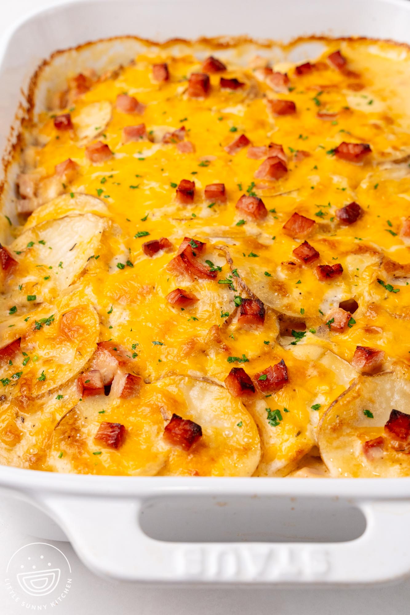 baked scalloped potatoes with ham and cheese in a white casserole dish.
