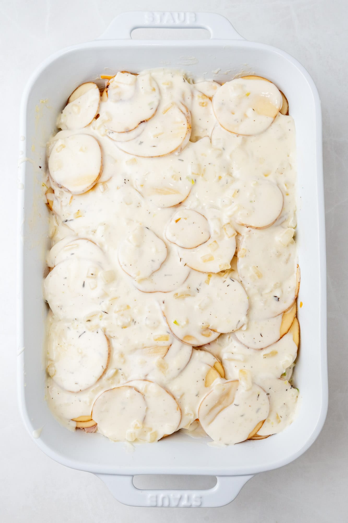 thinly sliced potatoes in a creamy sauce layered in a white ceramic baking dish