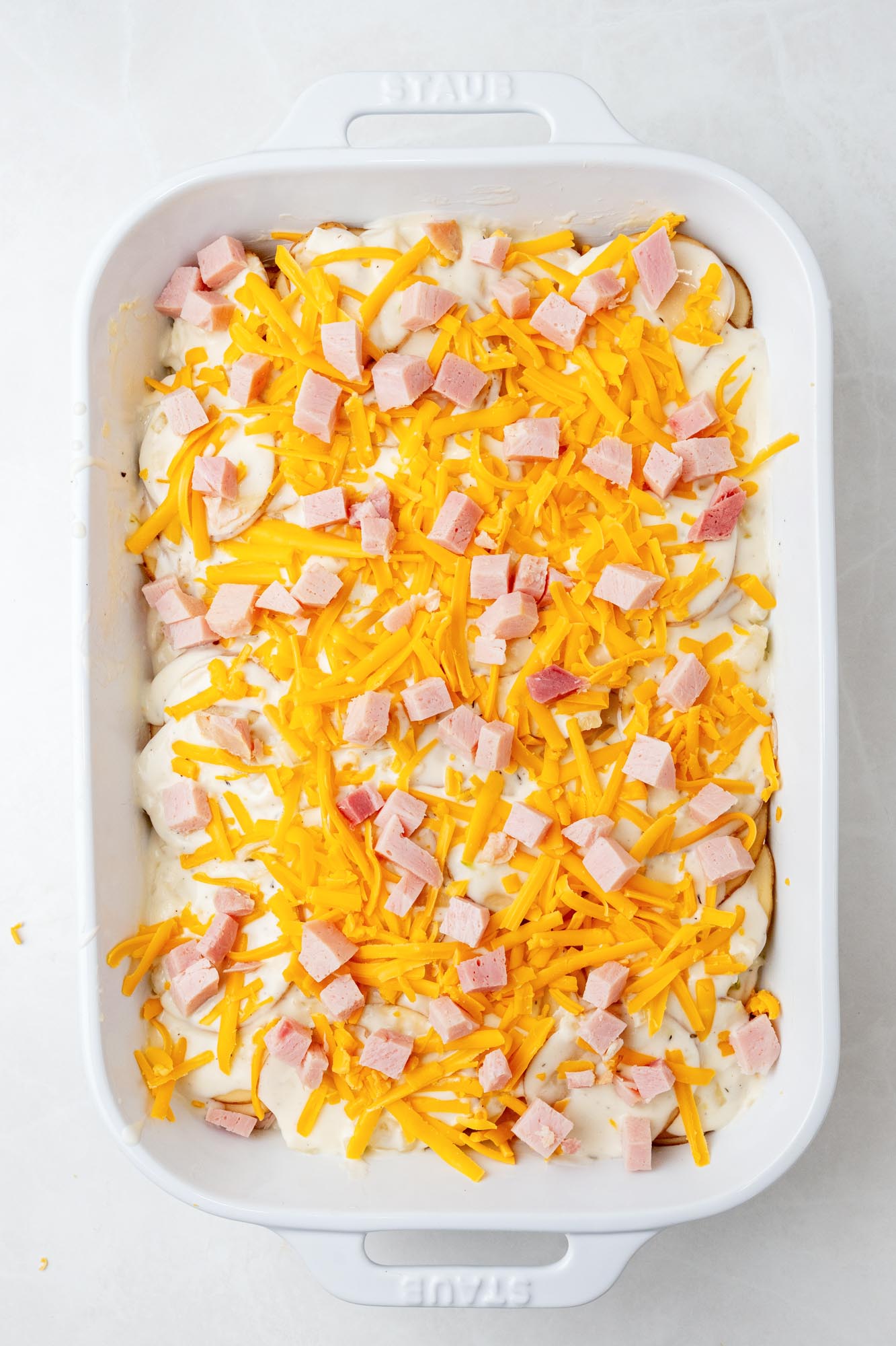 scalloped potatoes topped with diced ham and shredded cheese, before baking.