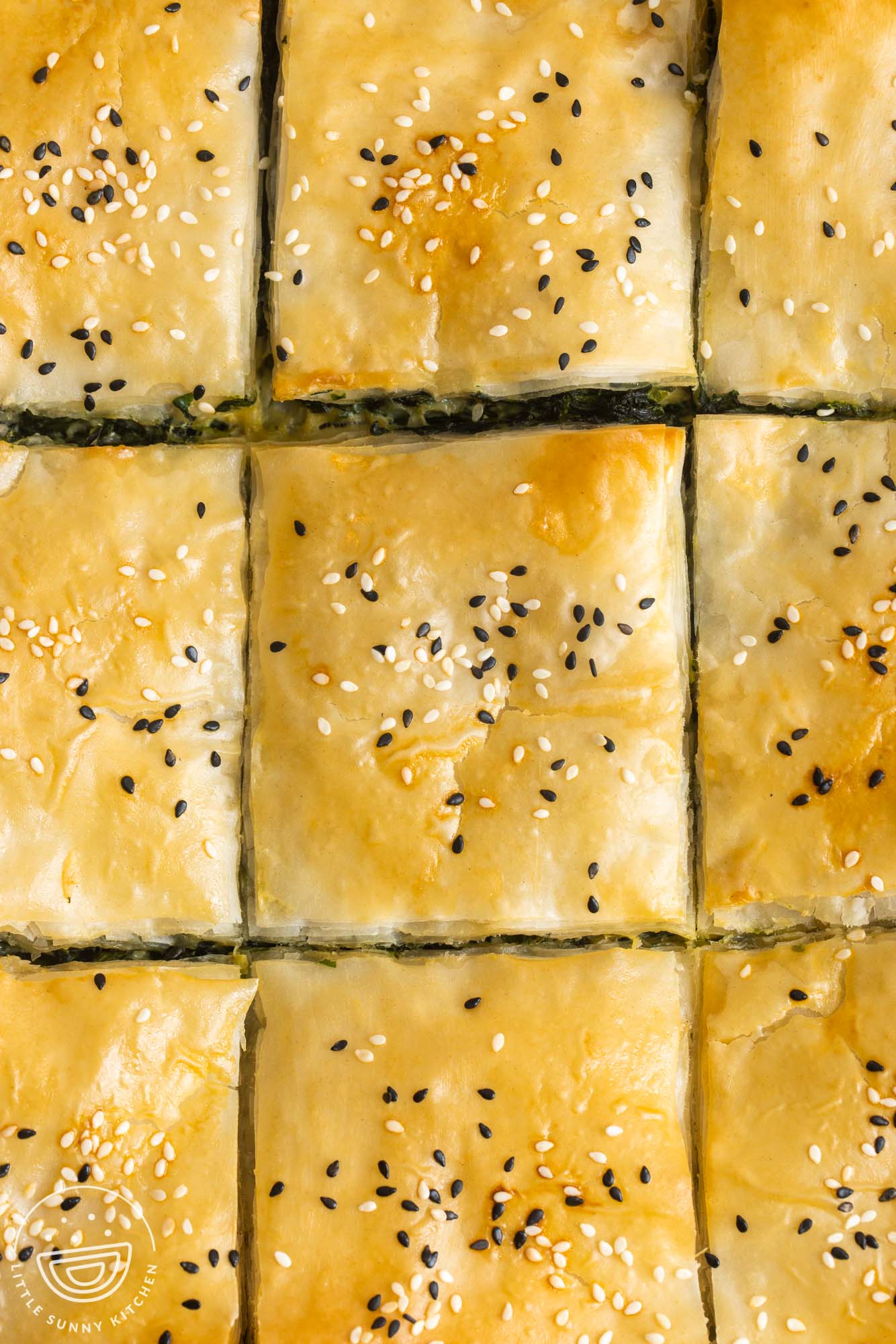 closeup of spanakopita sliced into squares, topped with sesame seeds