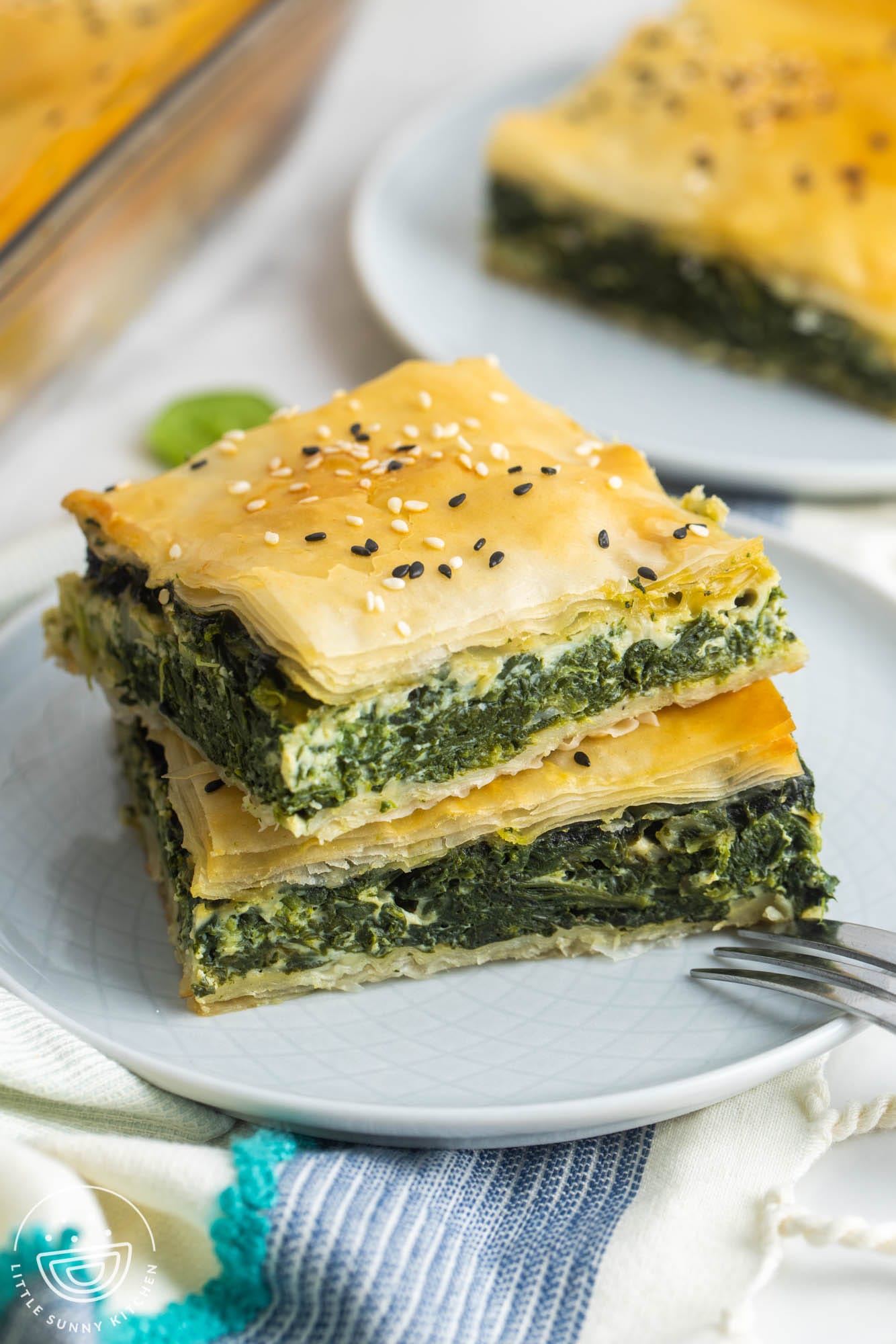 two squares of spanakopita on a gray plate with a small fork.