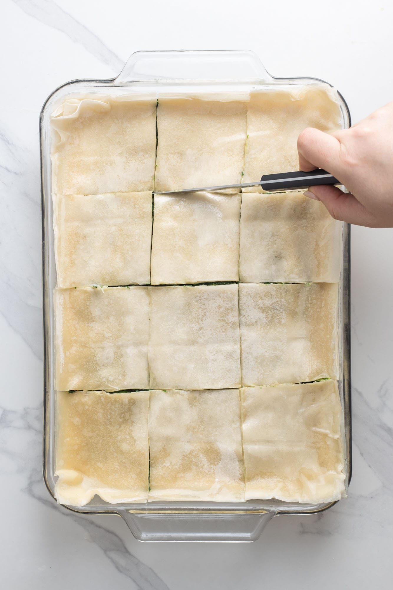 a hand using a knife to cute spanakopita into squares
