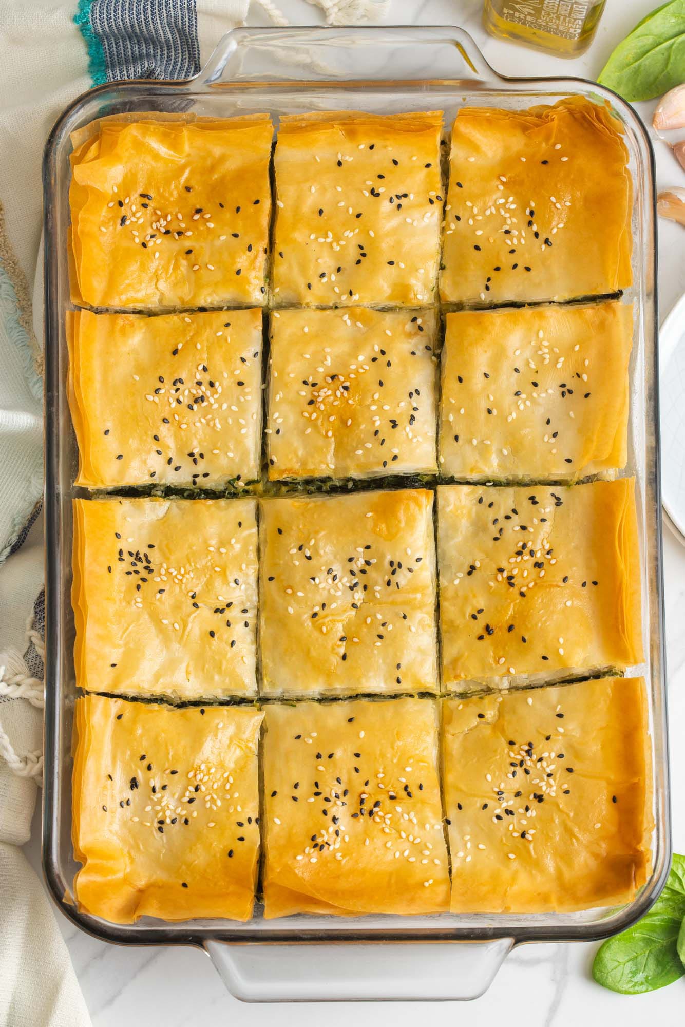 a 9x13 glass pan holding greek spinach pie, sliced into squares, golden brown.