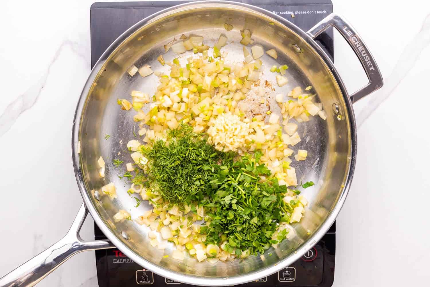 fresh herbs added to sauteed onions in a metal skillet.