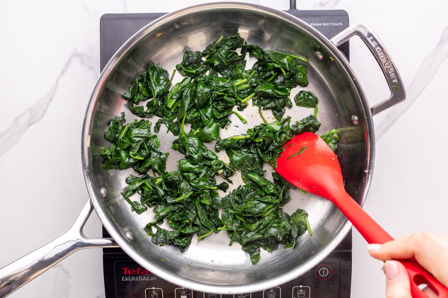sauteed spinach in a skillet stirred with a red spoon.