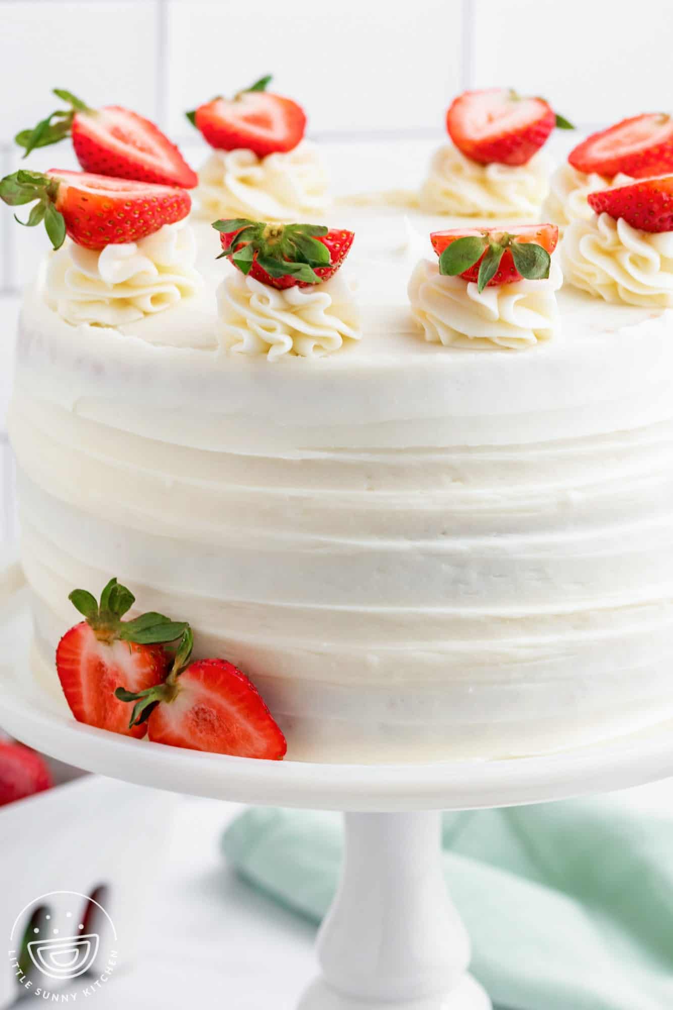 a whole round strawberry cake with white icing and fresh strawberries on top.