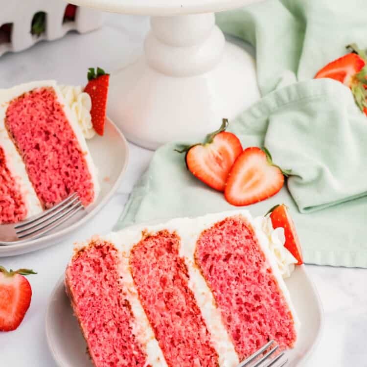 2 slices of strawberry layer cake on dessert plates with forks.