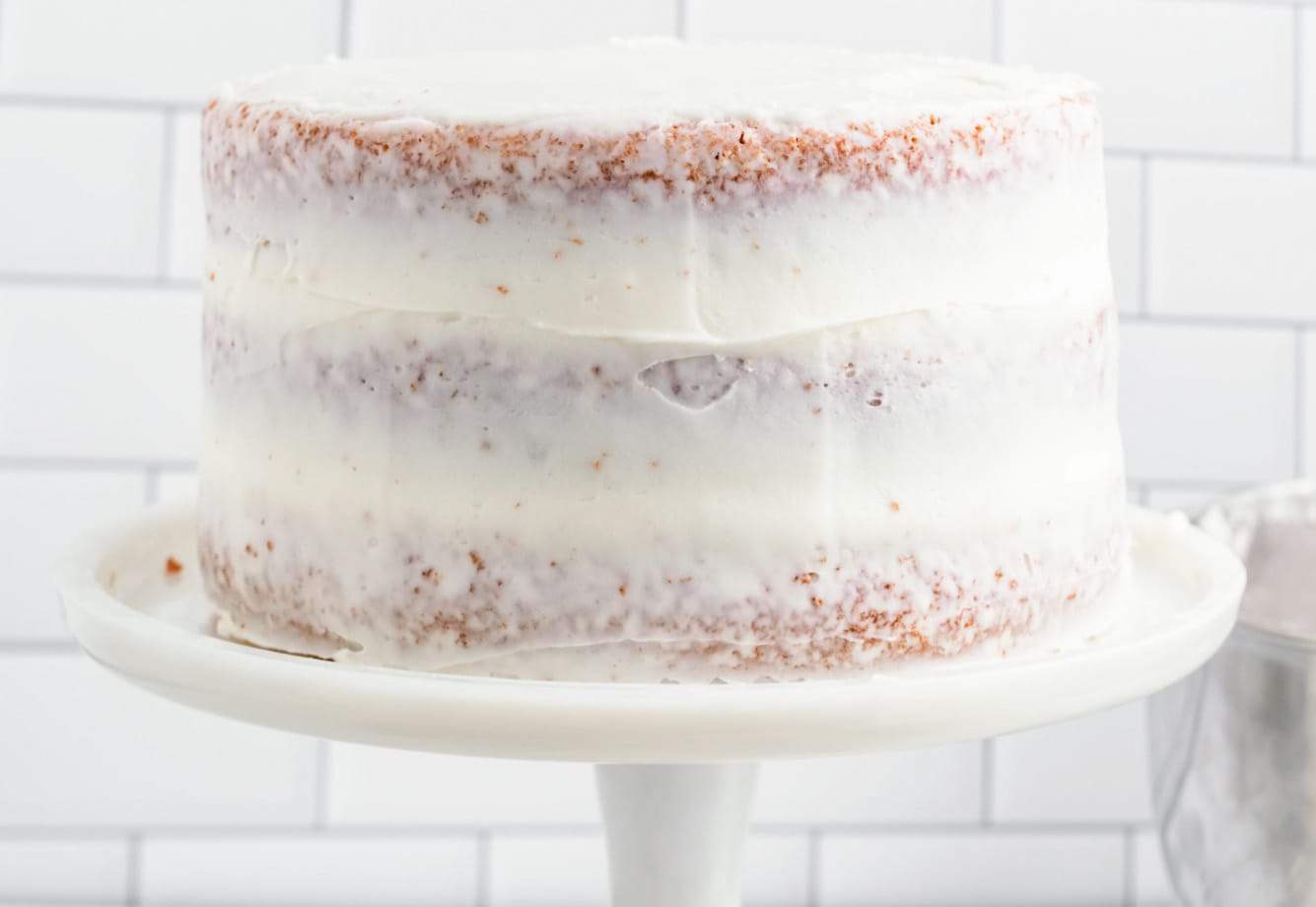 layer cake with crumb coat, on a tall white cake pedestal.