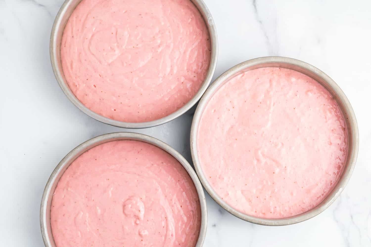 Strawberry cake batter divided into three round cake pans.