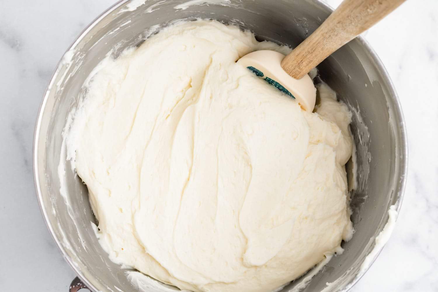 cream cheese frosting for strawberry cake in a mixing bowl with a spatula.