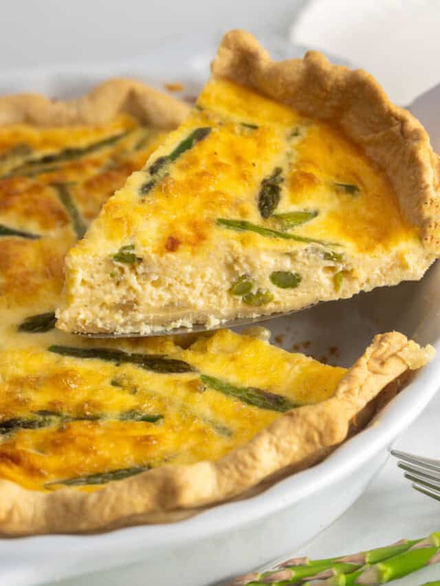 a slice of asparagus quiche lifted from the pan with a cake server.