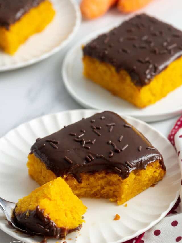 square slices of moist carrot cake with chocolate frosting on small white plates.