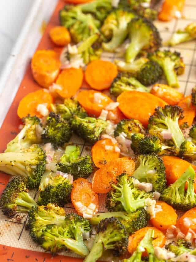 a grid silpat baking mat holding browned roasted broccoli and carrots, topped with shallots