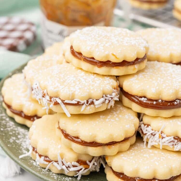 a green plate holding a stack of alfajores, dusted in powdered sugar