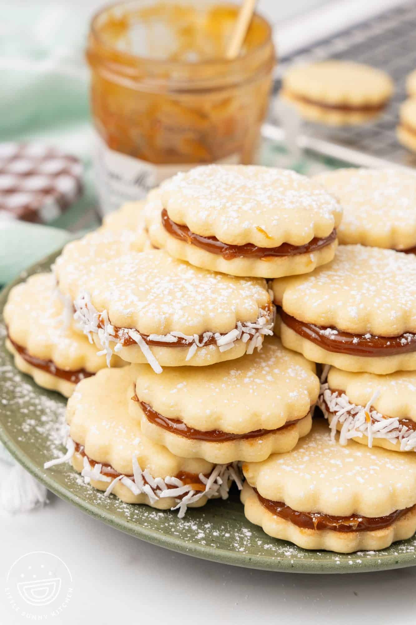 a green plate holding a stack of alfajores, dusted in powdered sugar
