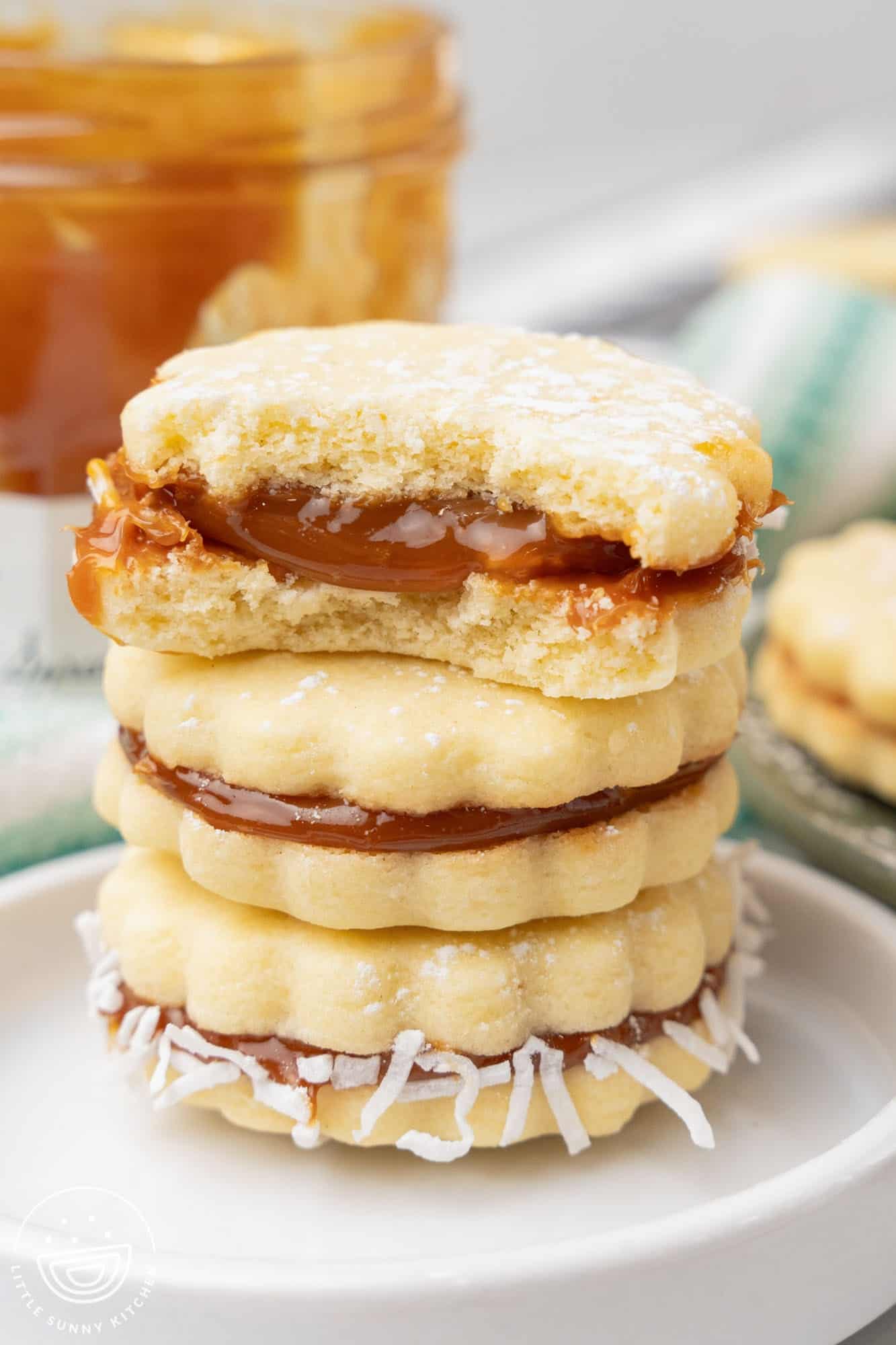 three alfajores cookies stacked. the top one has a bite taken to show the gooey dulce de leche inside