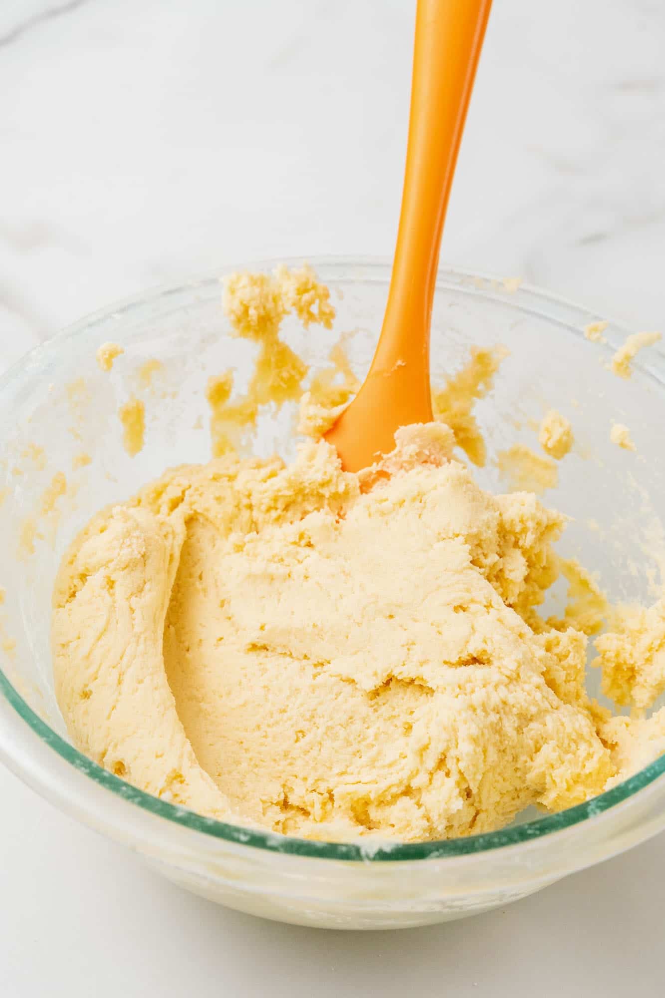 vanilla cookie dough in a glass bowl with an orange spatula.