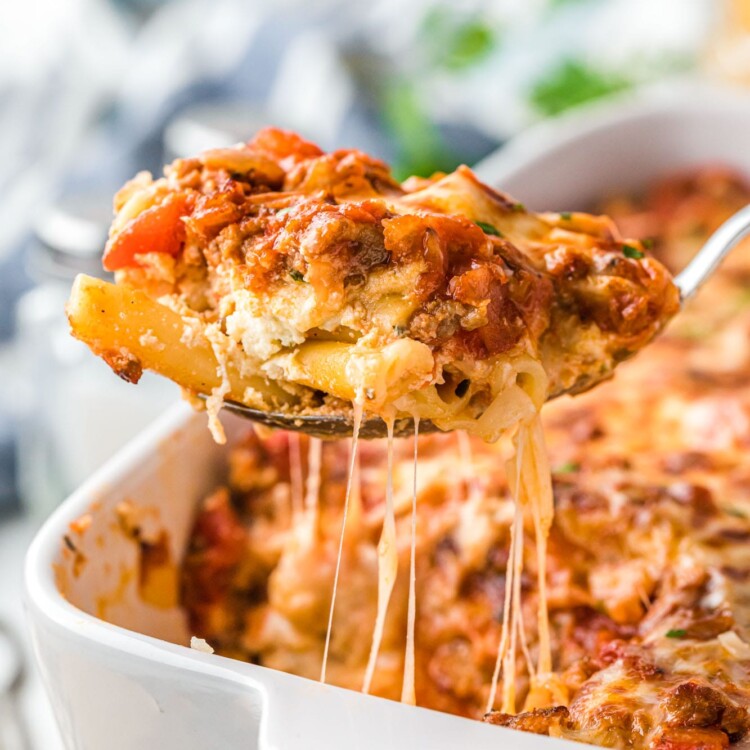 a spoon lifting up baked ziti from the pan, showing the melty cheese.