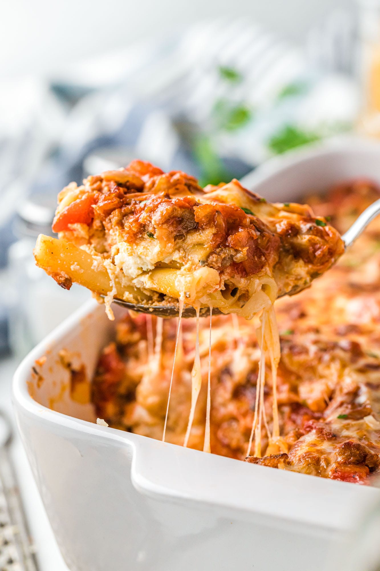 a spoon lifting up baked ziti from the pan, showing the melty cheese.
