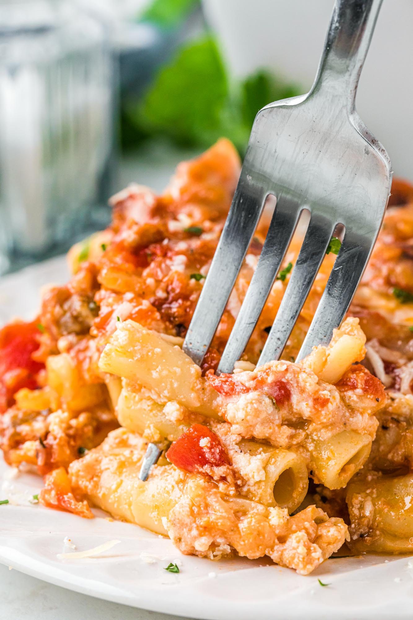 a closeup view of a fork eating baked ziti with ricotta cheese.
