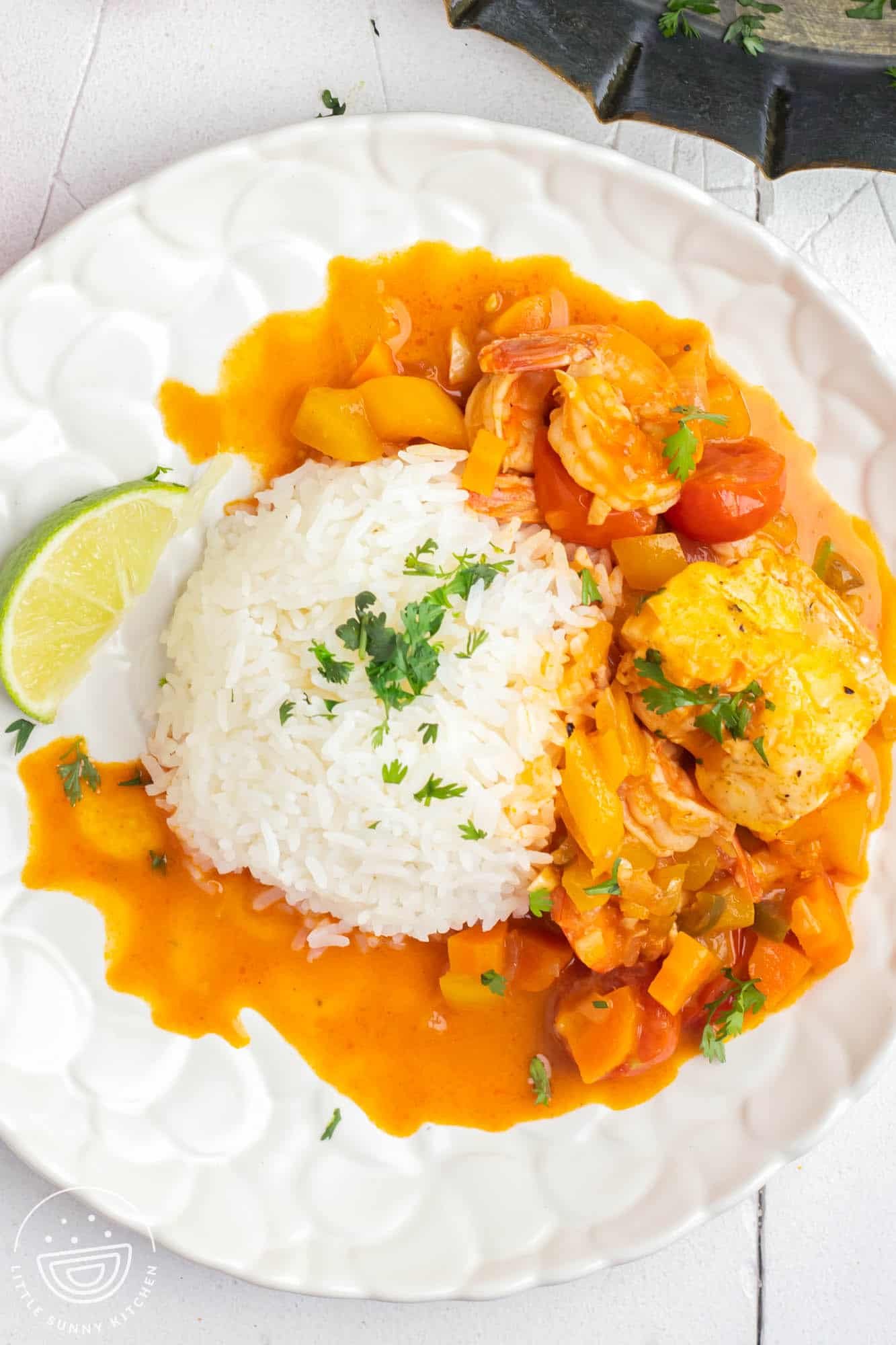a white textured plate of fish stew with white rice in the center