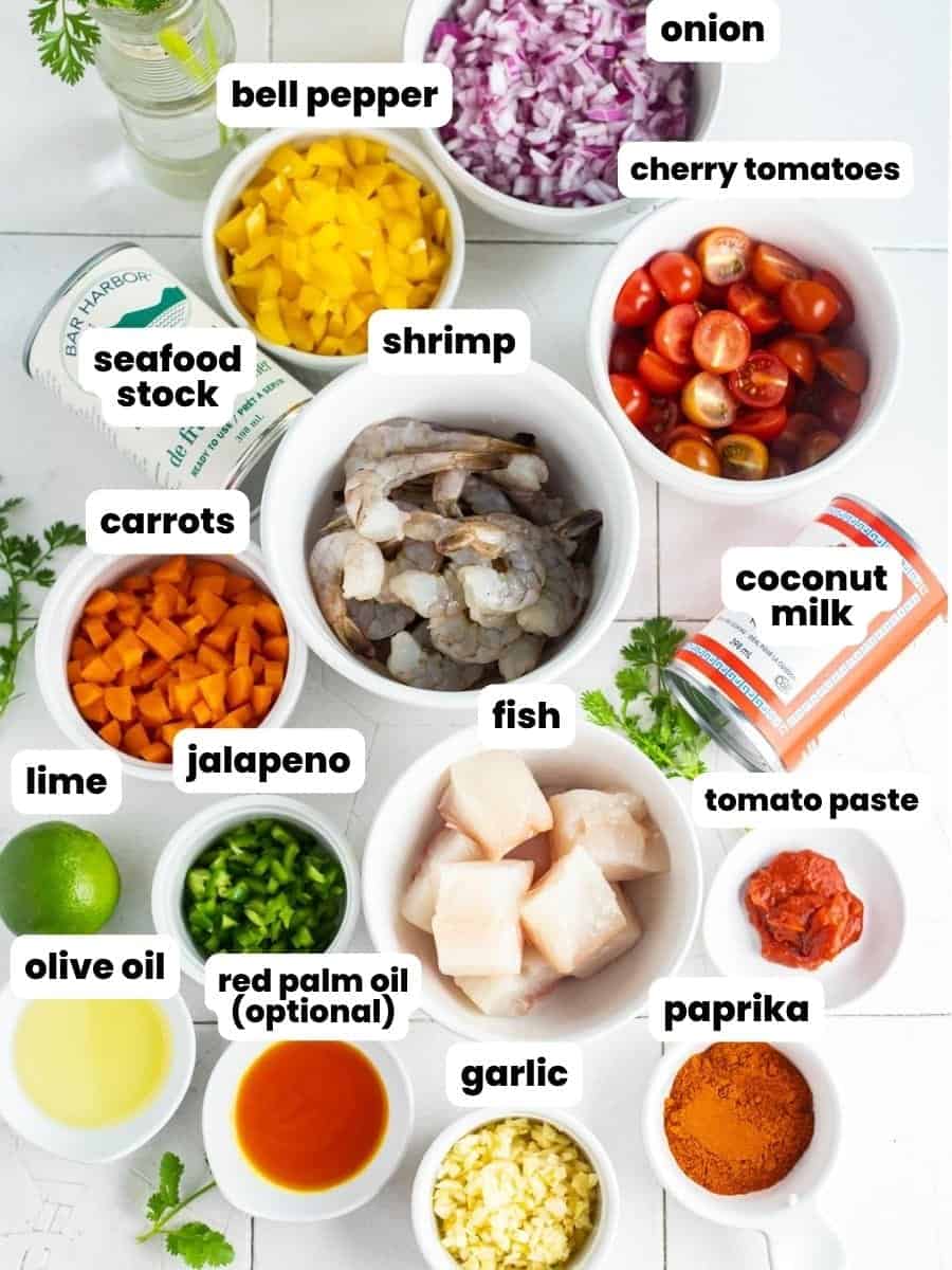 The ingredients needed to make brazilian fish stew including fish, shrimp, coconut milk, seafood stock, and vegetables, all arranged on a tile counter.