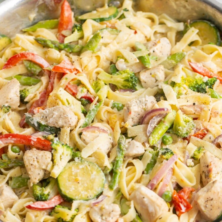 pasta primavera with chicken in a skillet, topped with grated parmesan