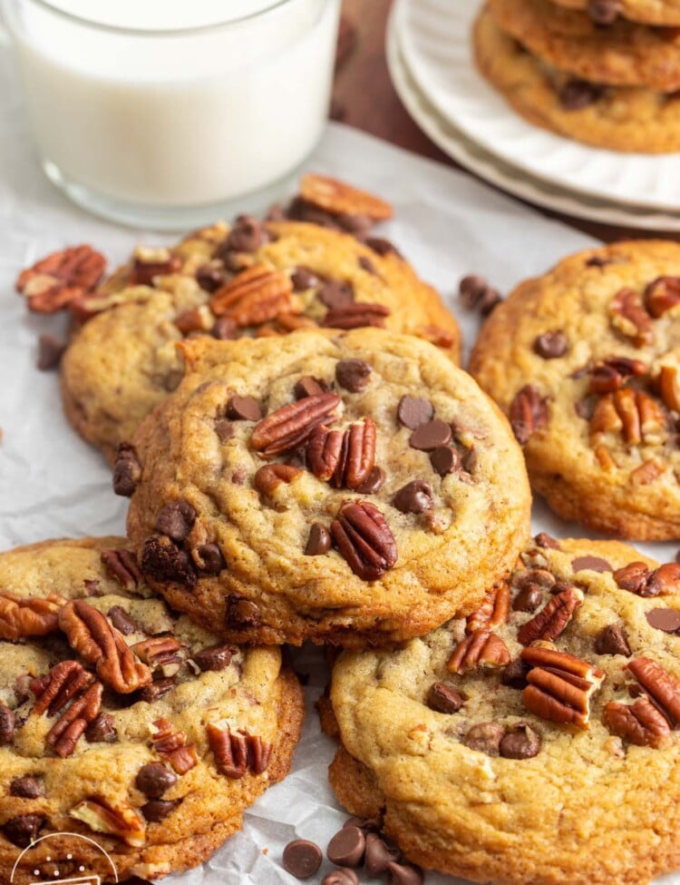 a stack of pecan chocolate chip cookies next to a glass of milk.