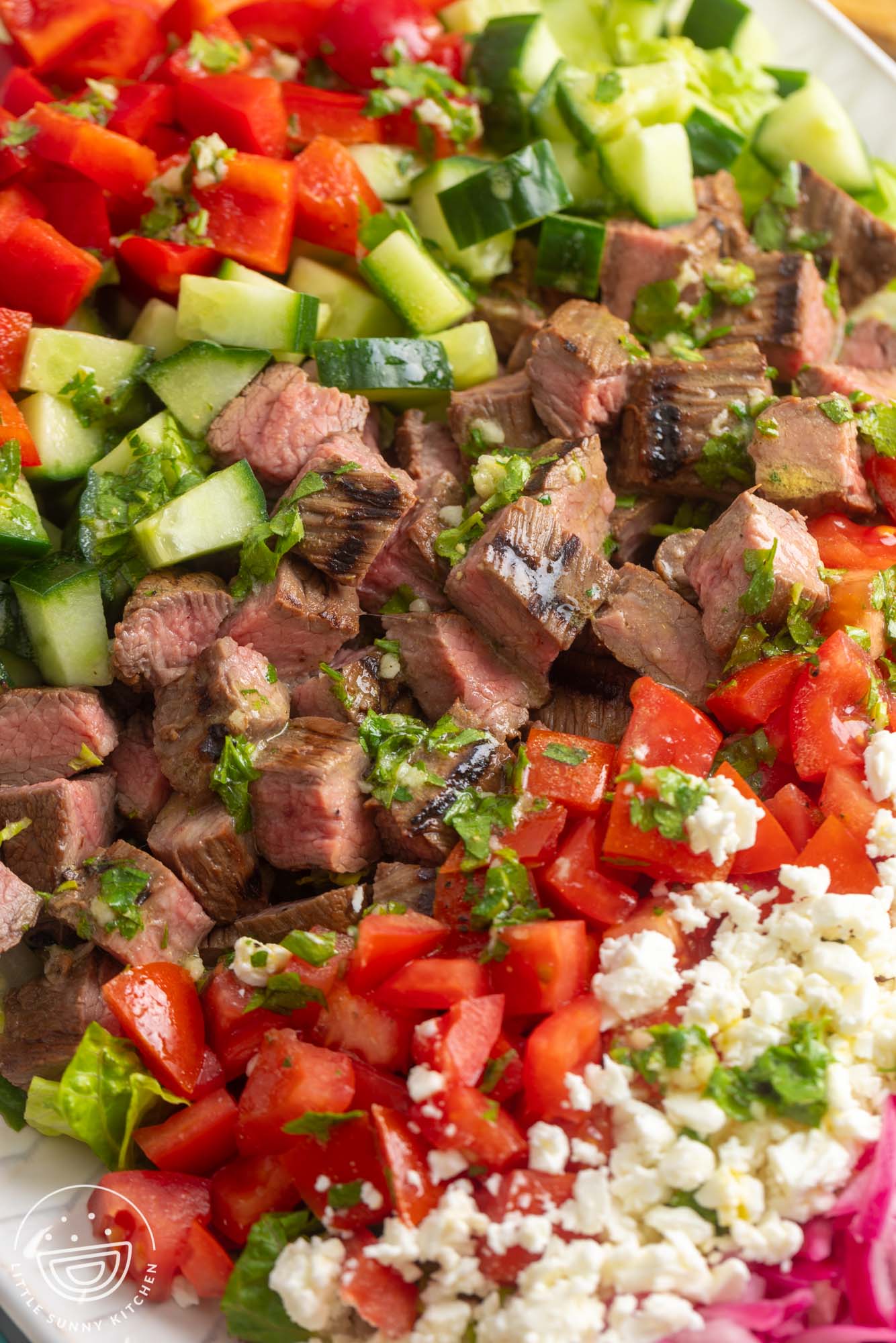 closeup of cubed grilled steak in a salad with tomatoes, red peppers, cucumbers and feta cheese.