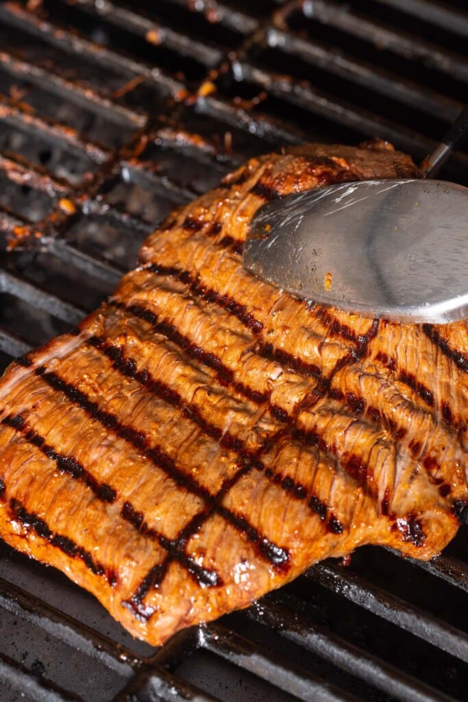 flank steak on a grill with grill marks, being flipped with tongs.