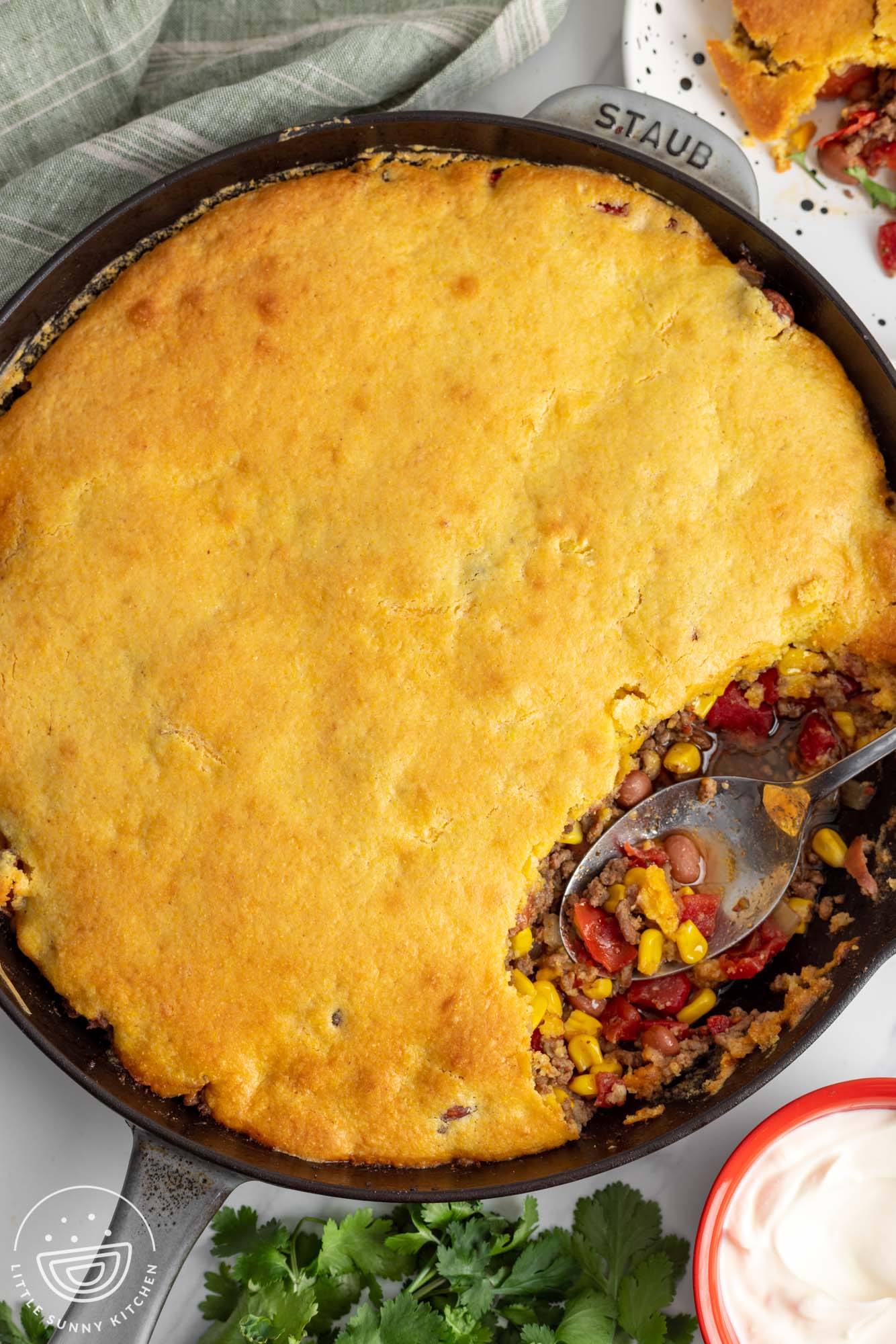 cowboy cornbread casserole in a large cast iron skillet. A spoon has removed one serving from the side of the pan.