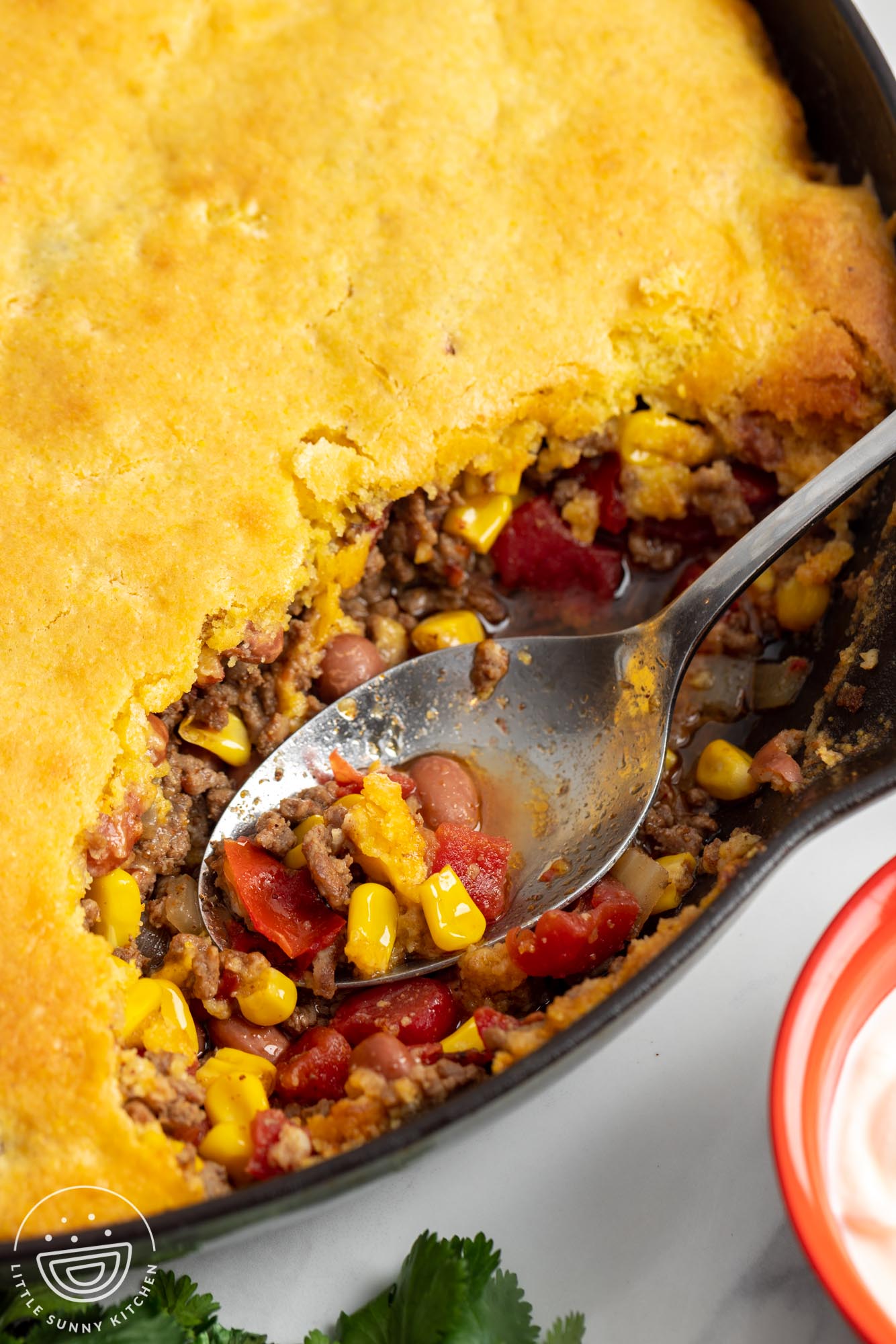 closeup of cowboy casserole in a skillet, made with corn, tomatoes, beans, and topped with cornbread.