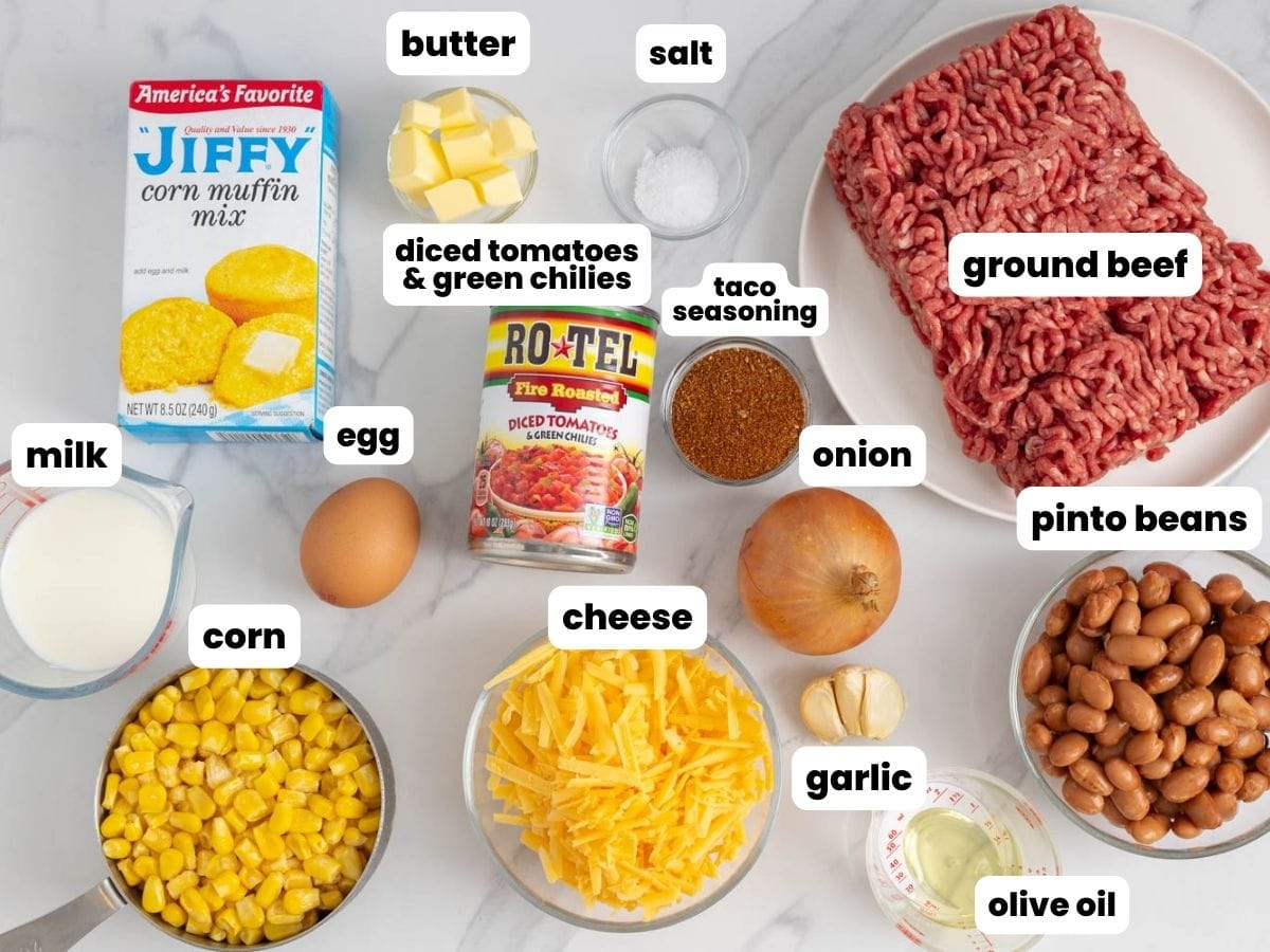Ingredients for cowboy cornbread casserole, including jiffy corn muffin mix, corn, and beef, arranged on a marble counter.