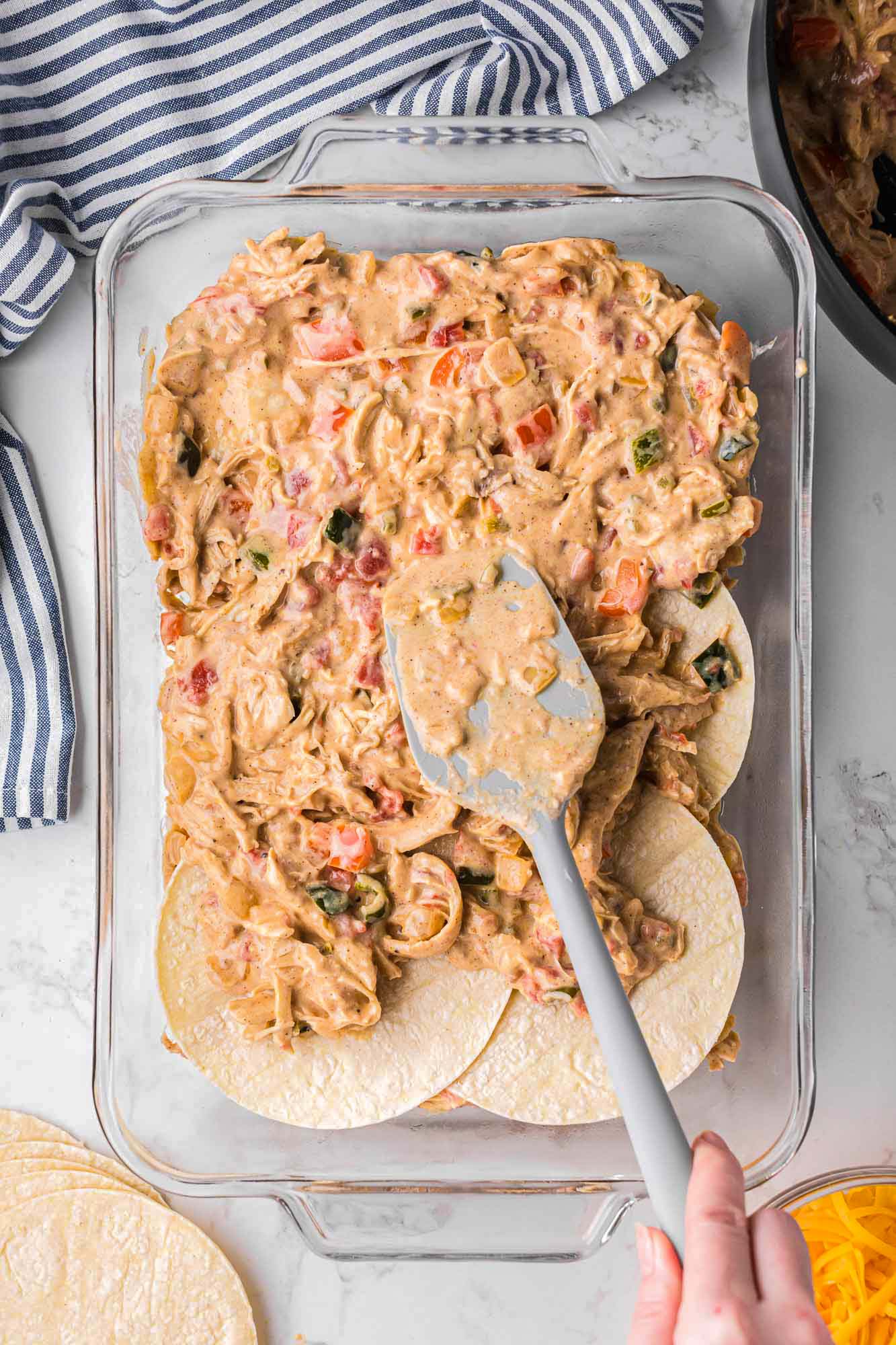 a layer of shredded chicken and veggies layered over tortillas in a casserole dish. 