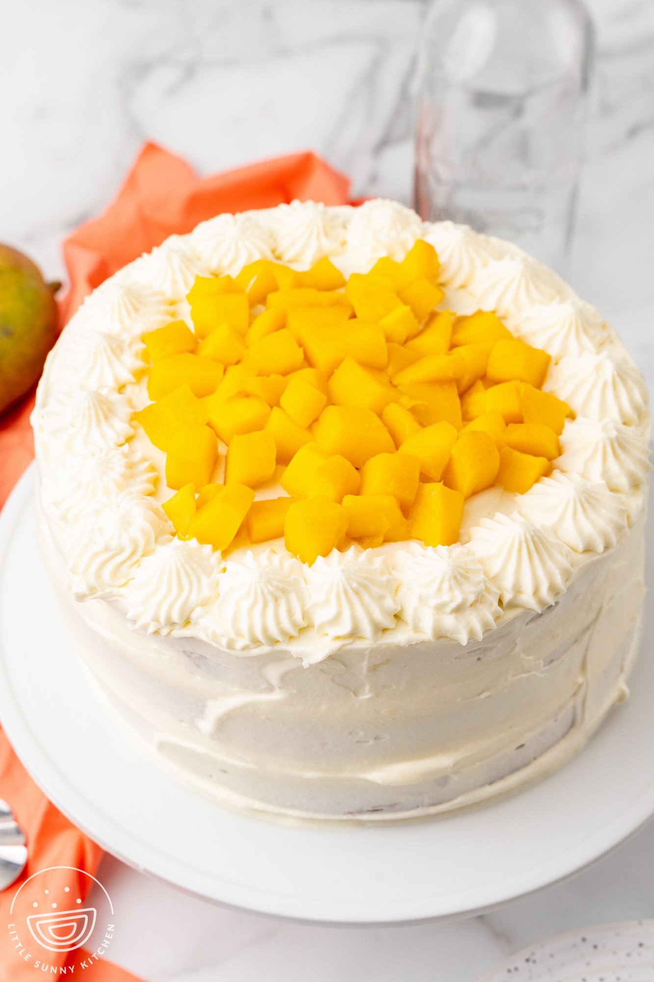 a round layer cake with white frosting, topped with fresh diced mangoes.