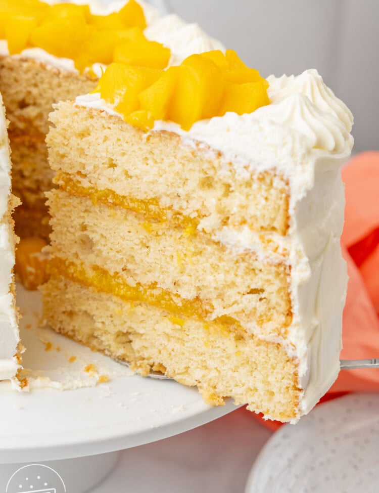 a slice of mango cake with frosting lifted away from the rest of the cake on a pedestal.