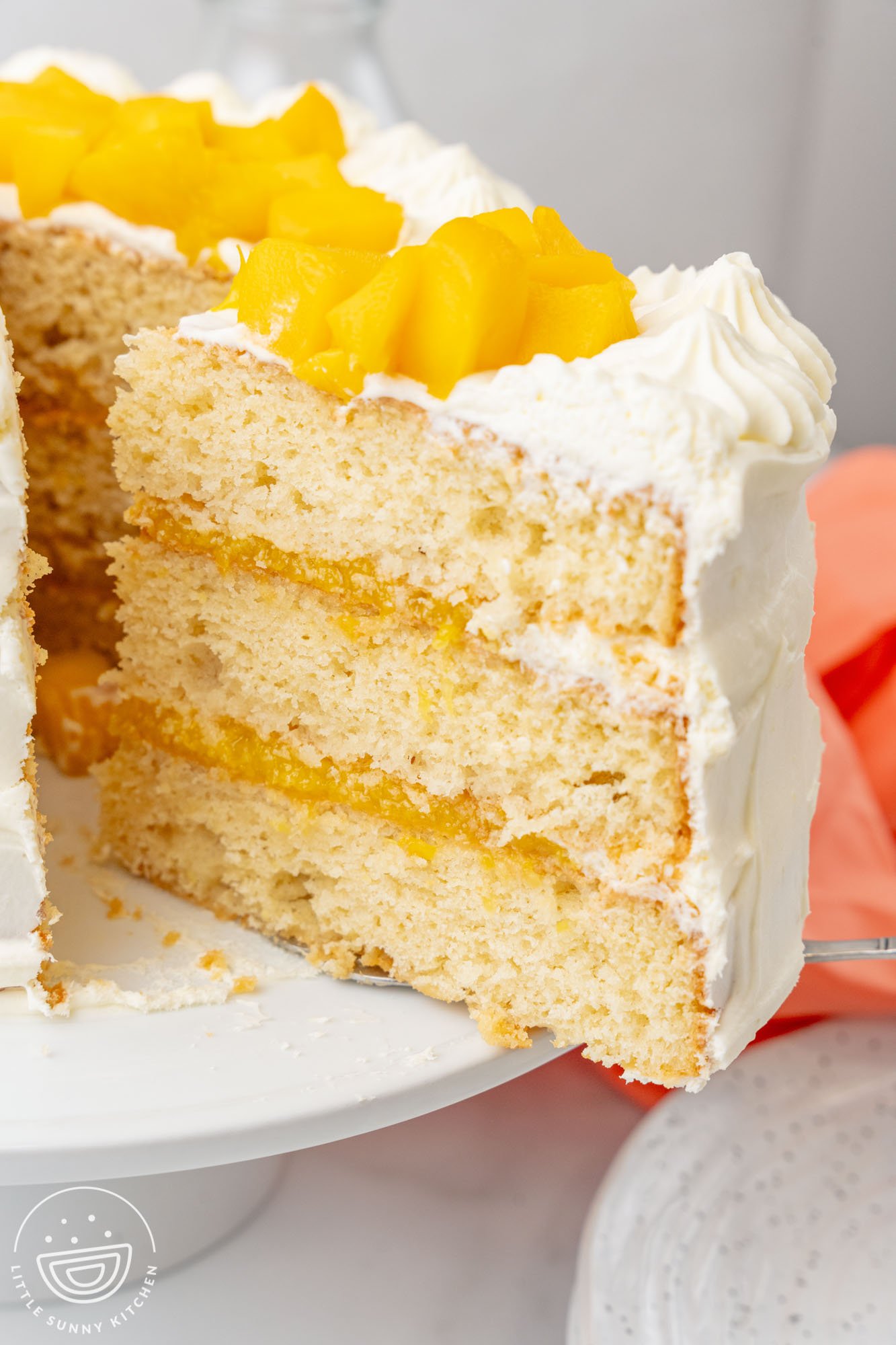 a slice of mango cake with frosting lifted away from the rest of the cake on a pedestal.