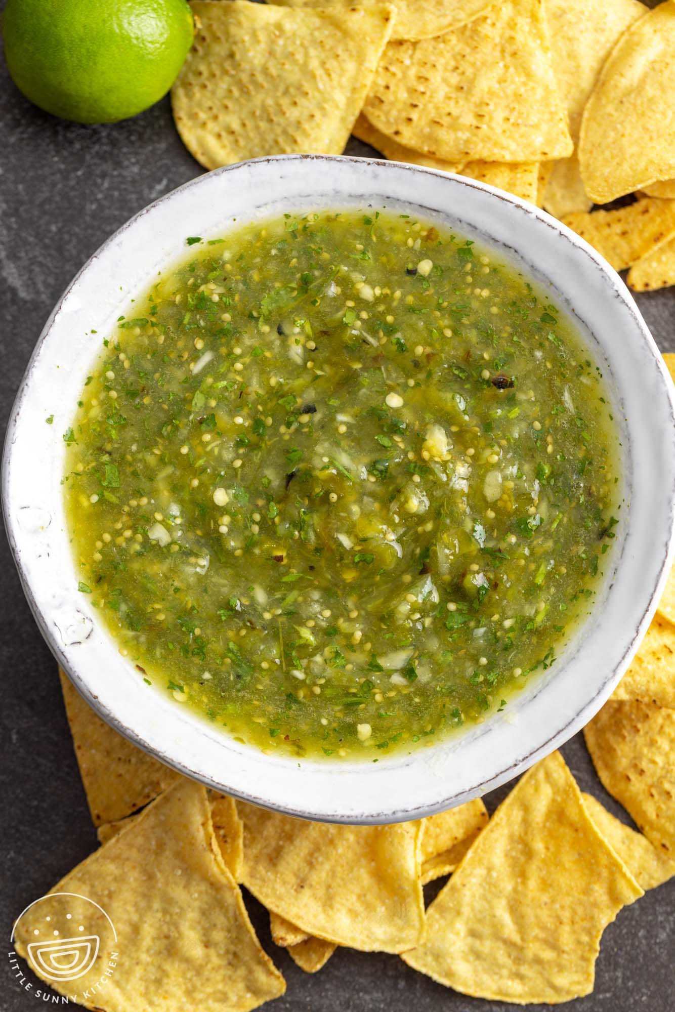 Overhead shot of a bowl filled with tomatillo salsa, and corn chips on the sides