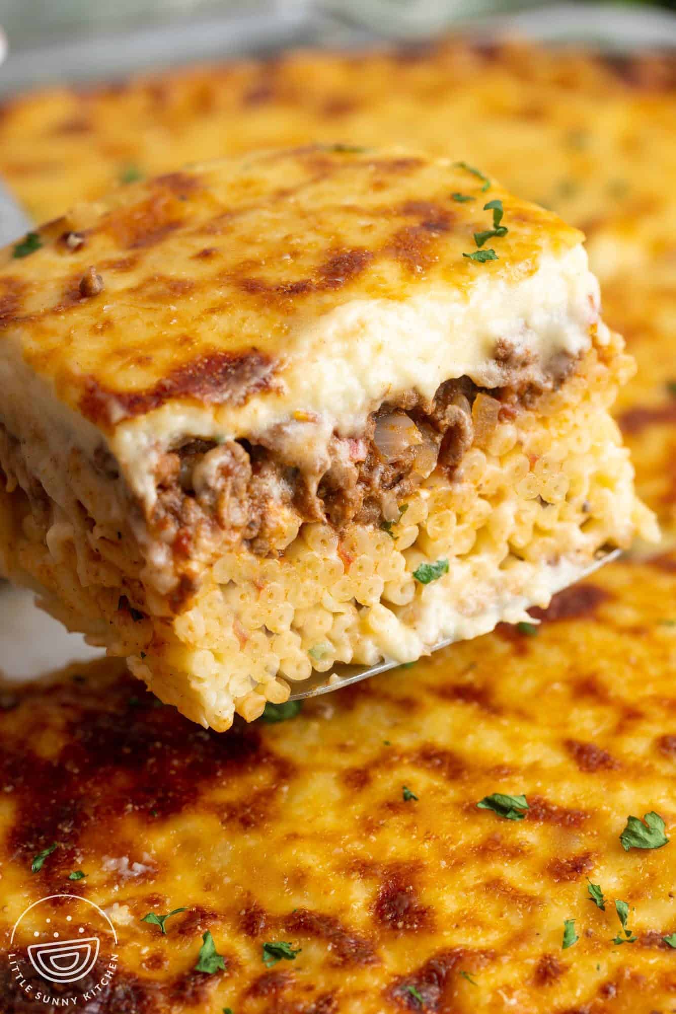 a square piece of greek pastitsio lasagna being lifted out of the pan with a spatula.