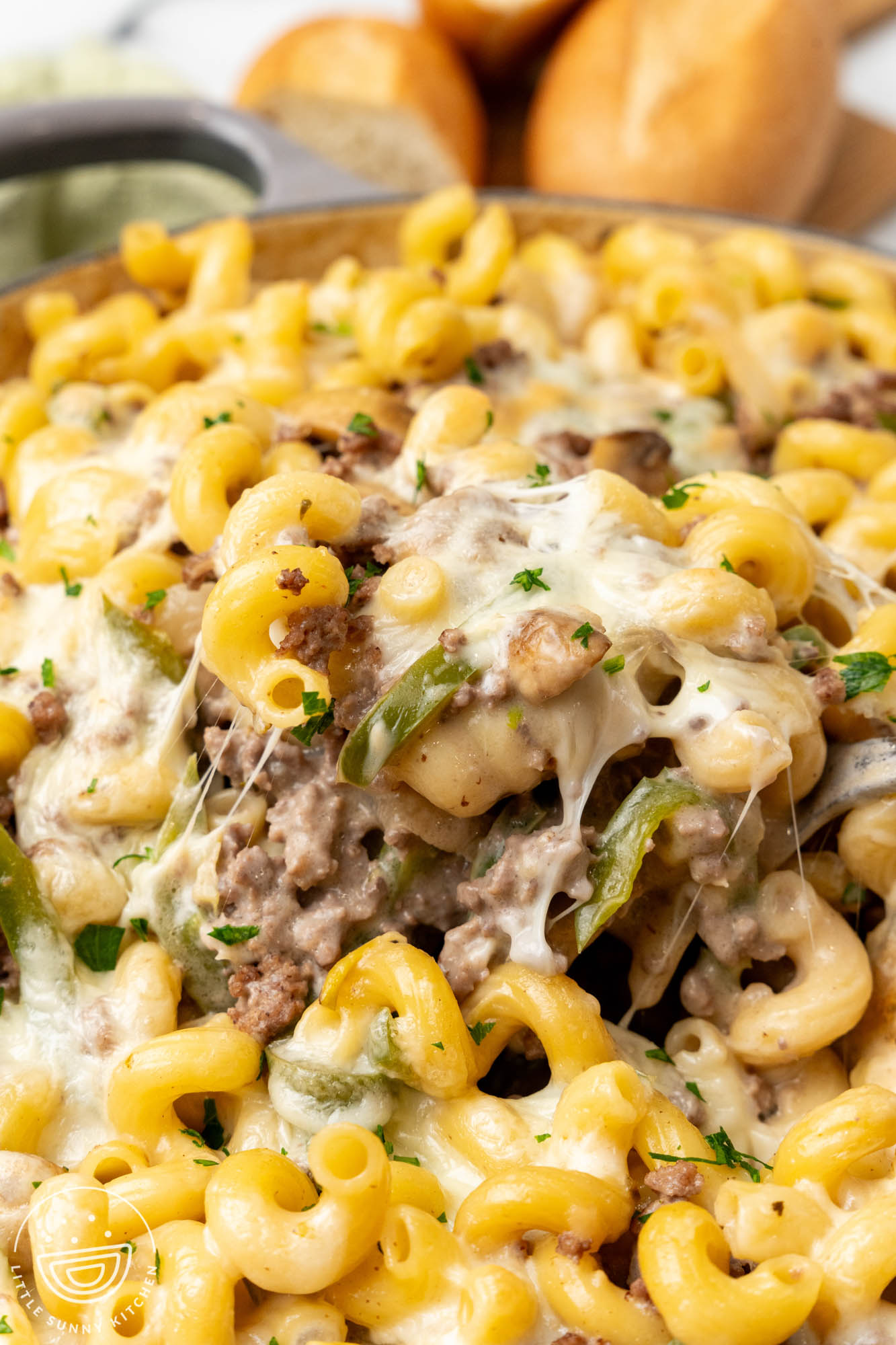 closeup of philly cheesesteak pasta. A spoon is lifting up a serving and the cheese is melty and stretchy