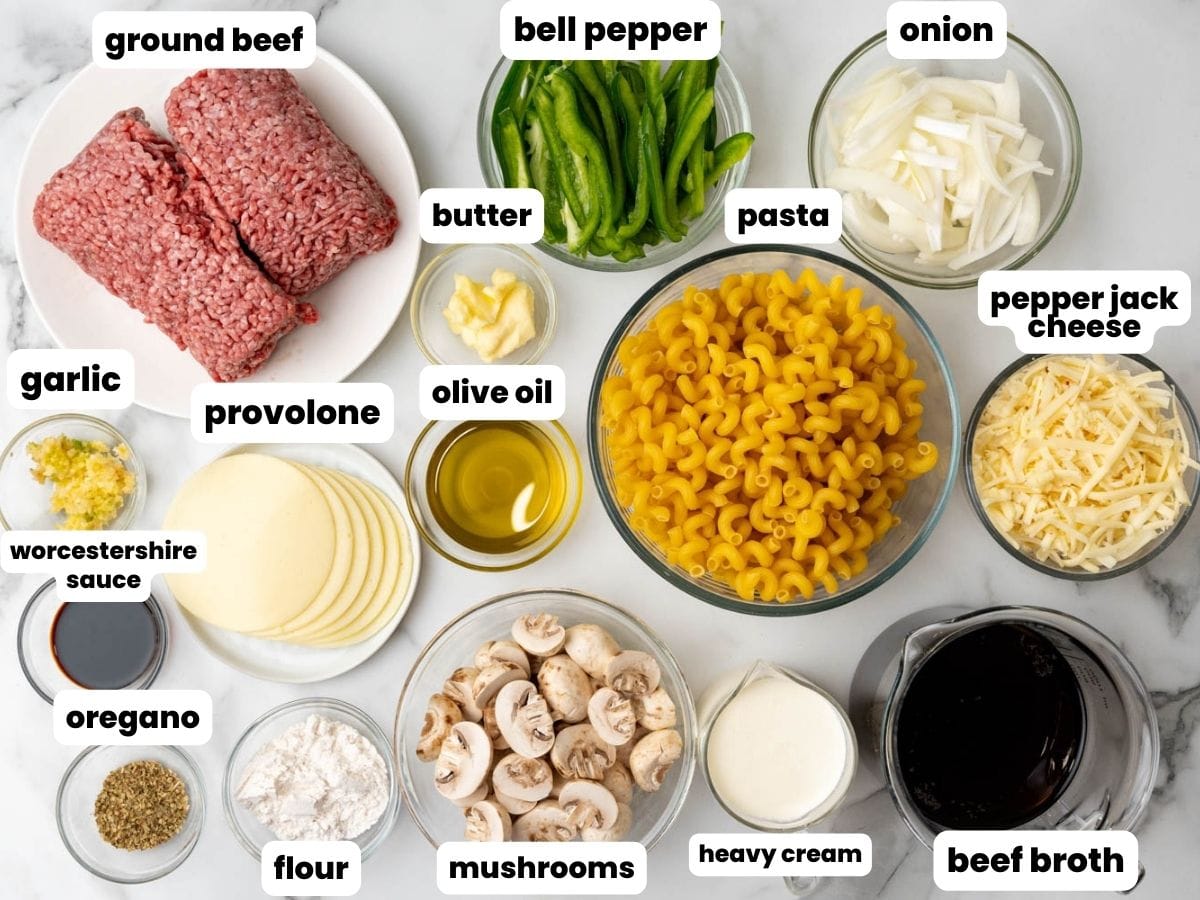 The ingredients for philly cheesesteak pasta including ground beef, provolone cheese, mushrooms, peppers, and onions.