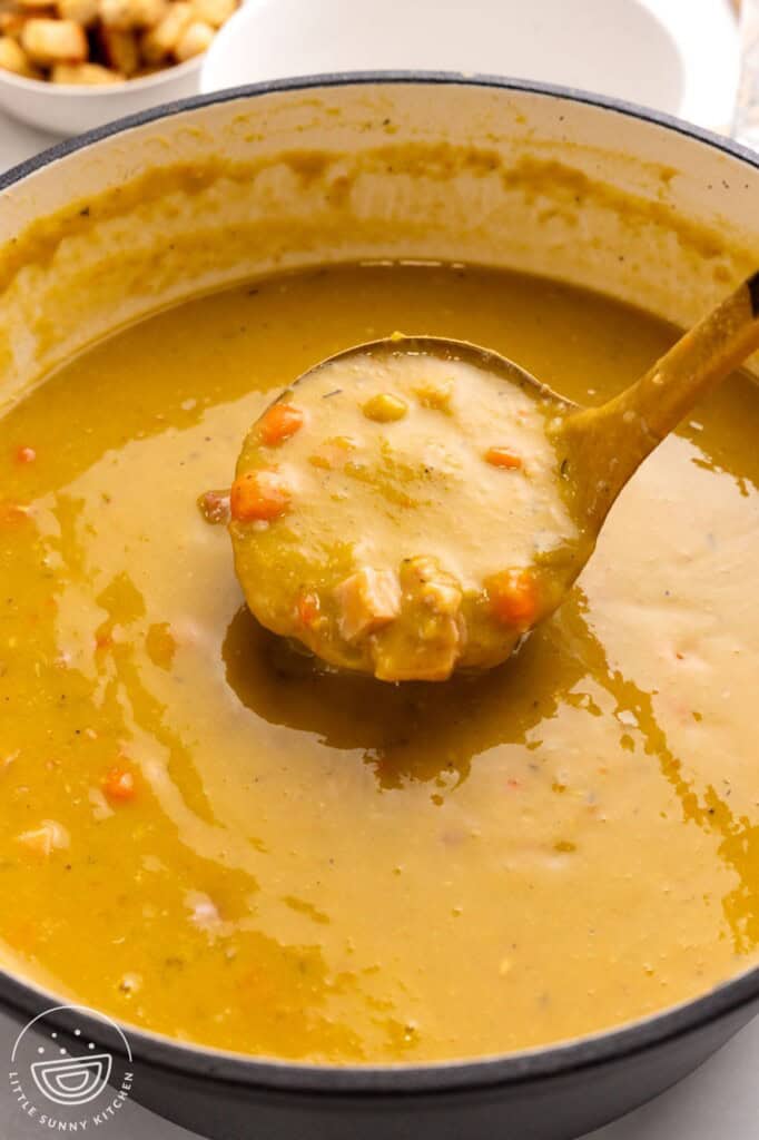 a black dutch oven of split pea soup. A ladle is picking up a serving.